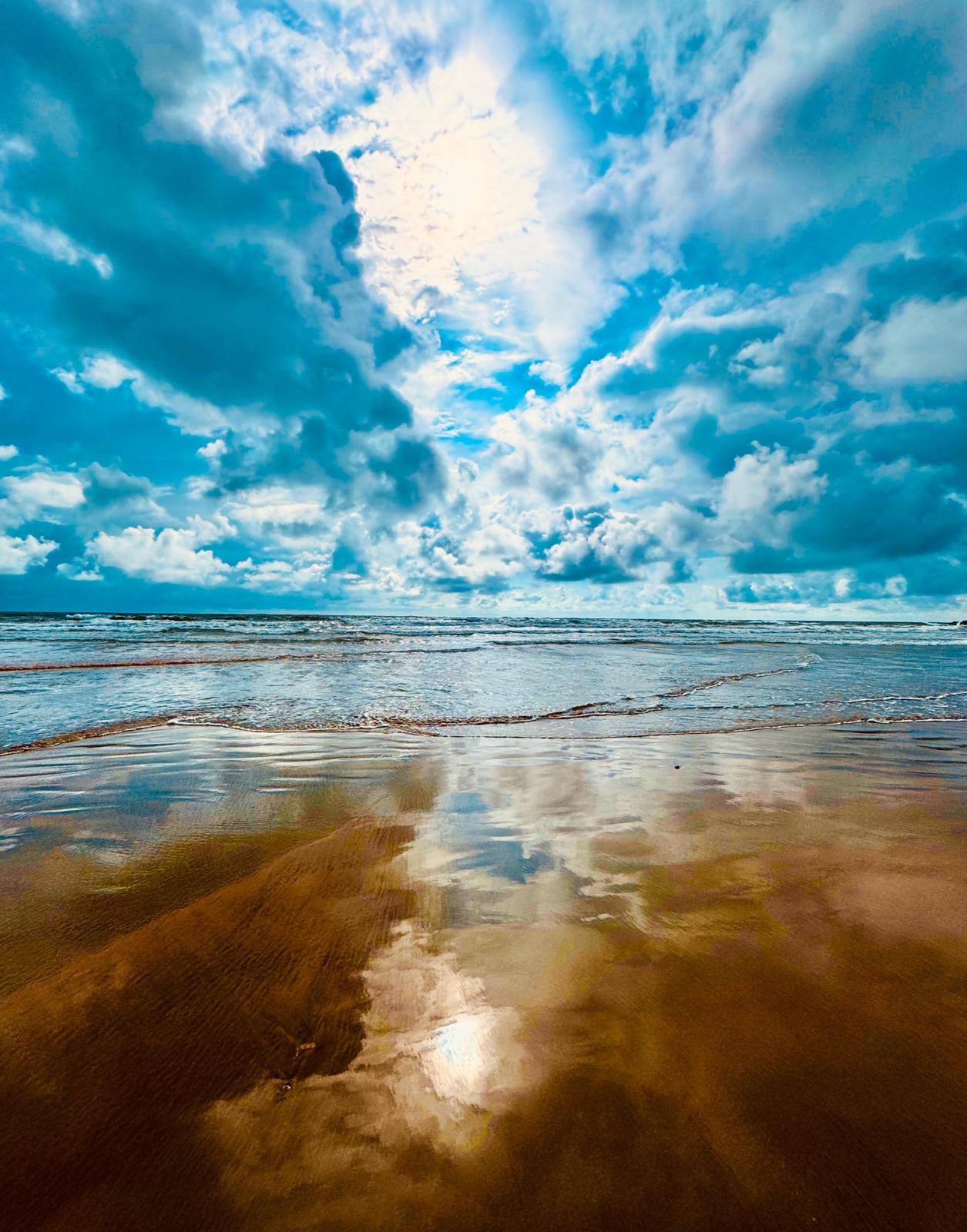 Sunlight breaking through clouds over a reflective beach