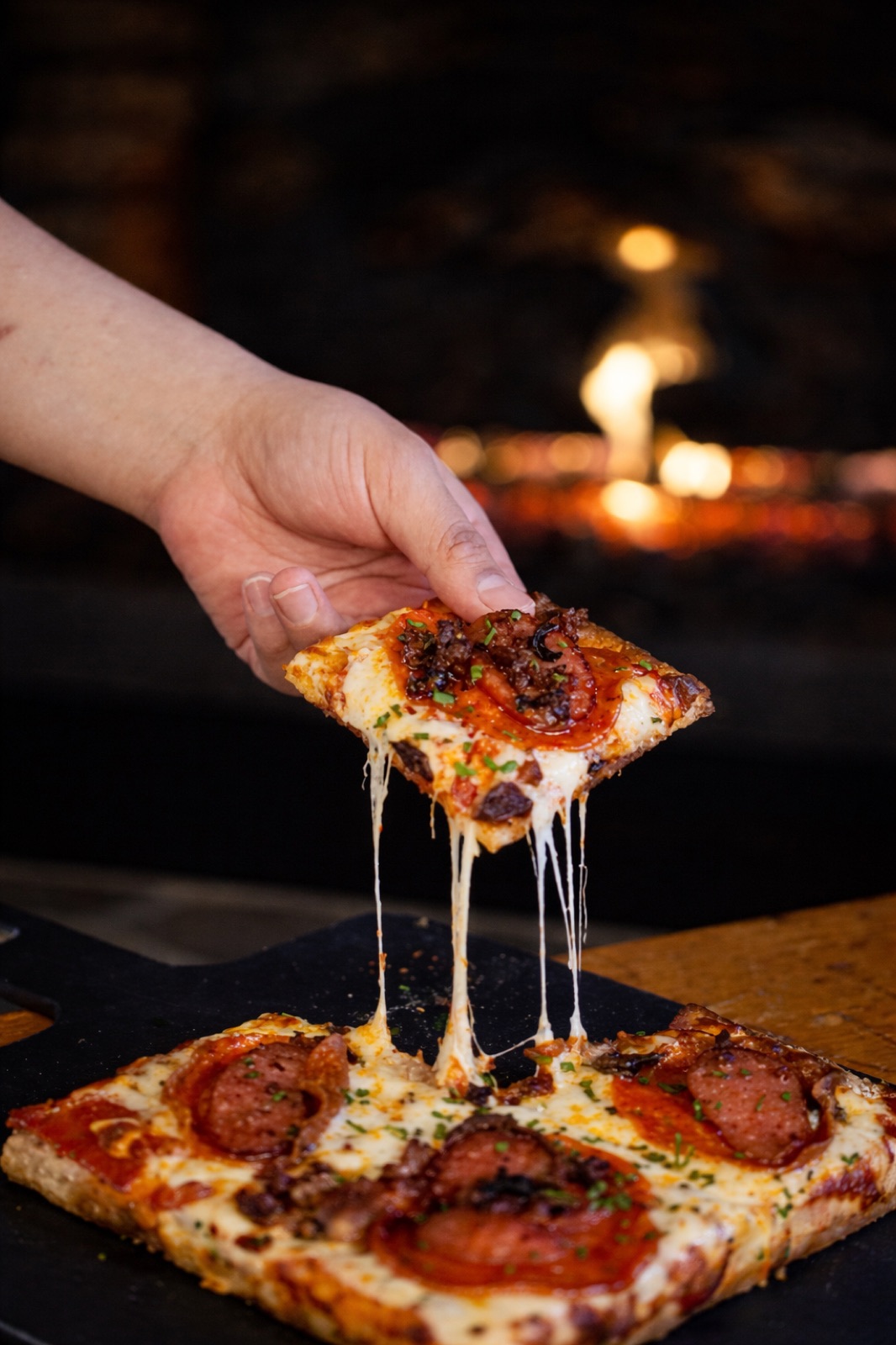 A slice of pizza lifted in front of a glowing oven