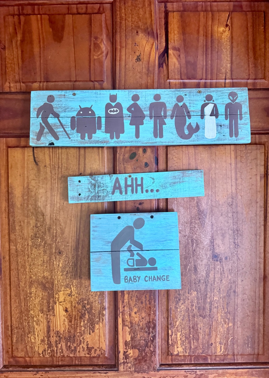 Playful inclusive restroom and baby-changing signs on a wooden door